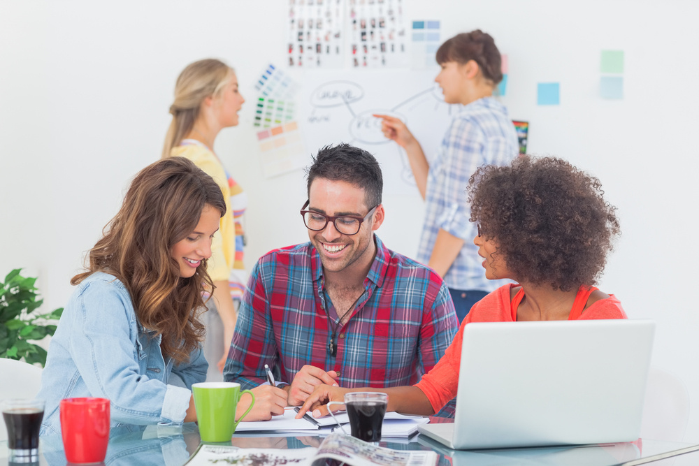 A diverse team of content creators collaborating on their next project. They are using laptops, notepads, and brainstorming on a whiteboard.